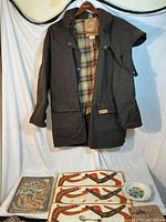 Full view of oilskin jacket open to show plaid lining; placemats, ashtray and other items laid out below
