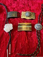 Group shot of three belt buckles and two bolo ties on red fabric