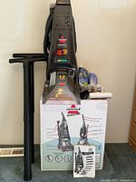 Full view of carpet cleaner standing on box with accessories and cleaning fluids