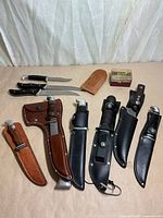 Group shot of hatchet, seven knives, boxed pocket knife and sheaths