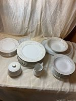 Stacked dinner and salad plates, bowls, platter, serving bowl, creamer and lidded sugar bowl on table