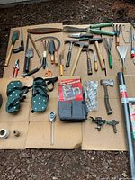Group of assorted garden hand tools, aerator sandals, tool organizer, sprinklers and hardware on cardboard