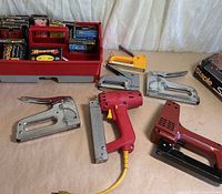 Overall lot: Arrow electric staple gun, Swingline electric stapler, four manual staple guns, organizer of staples visible
