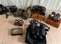 Group shot of eight binoculars, cases and Swift box