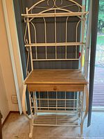 Full view of white metal bakers rack showing shelves, drawer, wood top