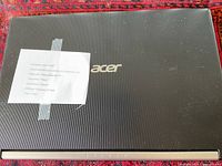 Top view of black Acer laptop closed, showing Acer logo and taped note on the lid.