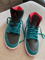 Pair of vintage Nike Air Jordan running shoes on a beige surface, turquoise, black and red colorway, showing worn condition.