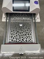 Front-loading chamber open with stainless steel perforated tray extended, touchscreen visible