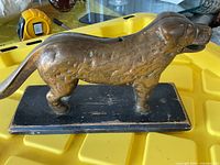 Brass dog shaped nutcracker resting on a yellow plastic tray with textured dog details and wooden base showing wear.