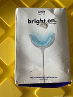 Photo of the front of the product box showing the bright on LED accelerator light and whitening pen with visible marks and wear on the box.