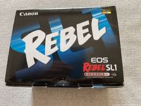 Front of box showing 'Rebel EOS Rebel SL1' branding and EF-S 18-55 IS STM kit designation