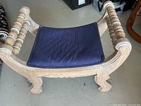 Full view of the wooden hall bench showing the turned spindle armrests, curved legs, and the navy blue seat cushion.