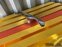 Polished metal abstract sculpture on a yellow and orange surface, showing side profile with smooth curved design.