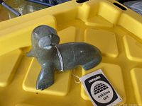 Photo of carved stone seal sculpture with tag Canada Eskimo Art on yellow surface.