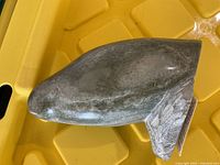 Side angled view of stone fish sculpture on yellow plastic surface