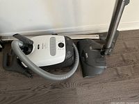 White and black Miele canister vacuum with hose and wand on hardwood floor