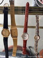 Four wristwatches displayed side by side with different straps including black leather, gold-toned mesh, brown leather, and silver-tone metal link.