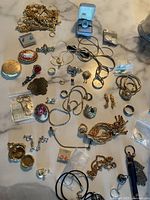 Top down view of a large collection of assorted jewelry on a surface including chains, brooches, rings, earrings, and pendants.