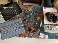 Wide view of the lot on a blue patterned textile, showing tablet with keyboard, sunglasses, jewelry, dog boots, and lens packet