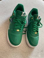 Top-front angled view of the green Nike Air Force One shoes showing lace detail and perforations on toe area.