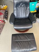 Full view of black leather swivel recliner and ottoman set on concrete floor