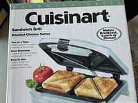 Photo of the front side of the box showing the open sandwich grill with two sandwiches inside, highlighting the product name and features.