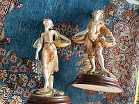 Two decorative statues on a patterned blue and red rug, showing details of the figures and bases.