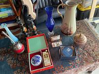 Overview of various decorative items on a patterned rug including vases, candle holders, trinket boxes, and a boxed apartment key holder.