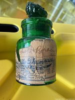 Front view of the vintage green glass apothecary bottle showing an ornate decorative stopper and worn label on the body.