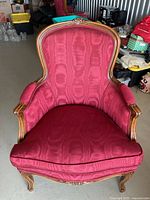 Front view of vintage upholstered armchair featuring carved wooden frame and red patterned fabric upholstery.