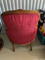 Back view of vintage upholstered chair showing red fabric upholstery and wooden frame with carved floral detail.