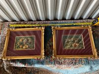 Two framed fruit prints laid flat on fabric surface, one frame shows visible damage at corners