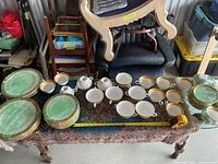 Wide view of wooden table showing three stacks of green marbled plates at left, rows of white cups in center, two sugar bowls and two creamers toward back right