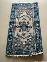 Full view of blue, cream, and black wool rug with geometric and floral design, showing overall condition and fringe ends.