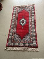 Full view of red wool rug with geometric patterns and fringed ends.