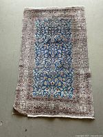 Full view of rectangular wool rug with blue floral center and cream decorative border, showing wear and creasing.