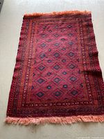 Full view of red wool rug with diamond pattern and fringed ends laid flat on floor
