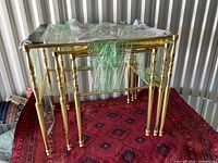 Set of three yellow brass framed nesting tables with glass tops on a red carpet, partially wrapped in plastic.