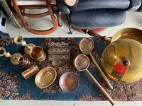 Various yellow brass items arranged on a patterned rug including bowls, candlesticks, a large lidded container, letter holder, and scoops.