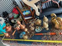 Wide view of multiple brass and copper items arranged on carpet showing variety including candlesticks, urns, and swan figurines.