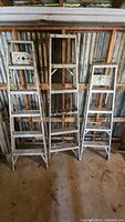 Three metal 5-step ladders leaning against wall