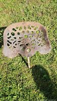 Top view of antique perforated cast iron tractor seat lying on grass