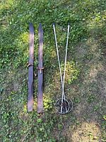 Full view of two wooden skis and two metal poles on grass