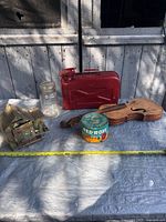 Group shot of all items: violin body, red jerry can, Mason jar, coffee tin, metal cabin sculpture, carved wooden piece