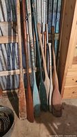 Group of nine wooden oars and paddles leaning against wall