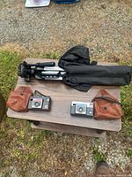 Overview of both cameras, leather pouches, folded tripod and carry bag on table