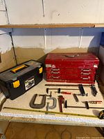 Overview of red tool chest, black toolbox, assorted clamps and tape measure on workbench