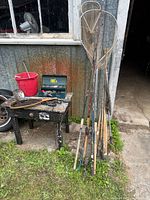 Group of fishing rods, two tall landing nets, bench with tackle box and bucket