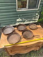 Five rusted cast iron skillets on wooden surface with tape for scale