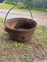 Full view of cast iron cauldron resting on ground showing bail handle and interior